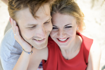 young couple sitting on the sand smiling and hugging