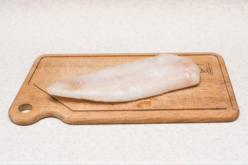 Frozen and thawed fish fillet on the cutting board on the kitchen table