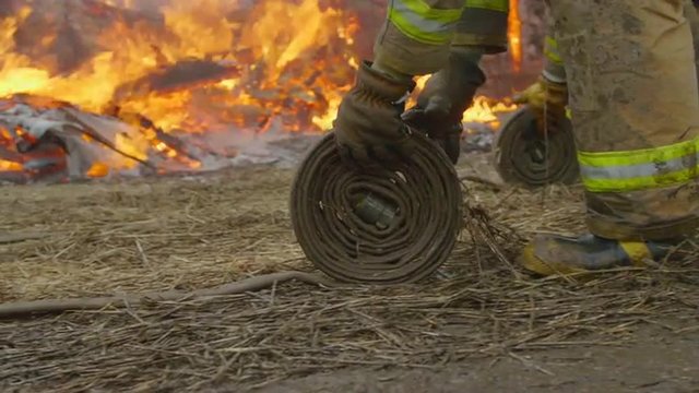 Done with their job, a couple of firefighters wrap up their water hoses as a house continues to smolder in the background