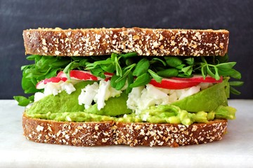 Superfood sandwich with whole grain bread, avocado, egg whites, radishes and pea shoots on marble against a black background © Jenifoto