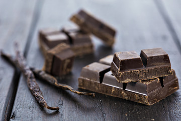 Chunks of dark chocolate bar and vanilla beans on wooden table
