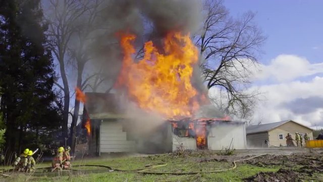 Firemen spray water on a burning house from the front and back 