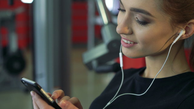 Young smiling woman at the gym listening to music using a mobile phone.