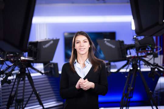 Television Presenter Recording In Television News Studio.Female Journalist Anchor Presenting Business Report.News Camera,light Equipment Behind The Scenes.Talking At Camera To The TV Audience