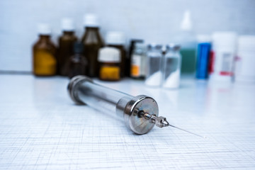 Vintage syringe with glass vials and medications pills, drugs in background