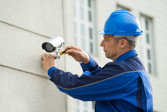 Mature Technician Installing Camera On Wall With Screwdriver