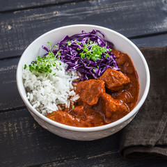 Stewed meat in tomato sauce, rice, red cabbage  on a dark wooden table. Delicious healthy lunch