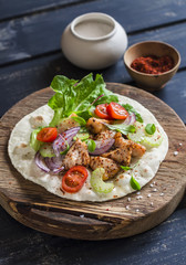 Delicious grilled chicken and fresh vegetables homemade tortilla on a rustic cutting board on a dark wooden background