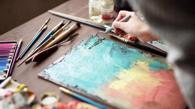 artist paints a picture of oil paint brush in hand with palette closeup.