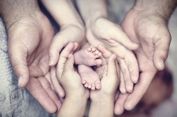 Руки отца, матери, дочери, держать ножки малыша. Дружелюбная счастливая семья, руки вместе

