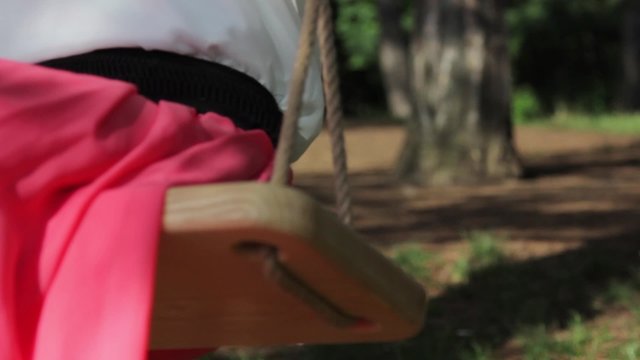 Pretty girl in a pink dress riding on a swing