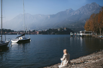 Fototapeta na wymiar girl sitting on the shore of a mountain lake Como with yachts