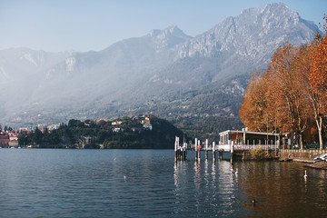 Fototapeta premium Pier and autumn trees on the shore of a mountain lake Como
