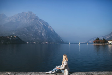 blond woman in coat sitting against the background of a mountain lake Como