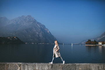 Fototapeta na wymiar blond woman in coat standing against the background of a mountain lake Como