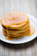 Stack of homemade pancakes with honey on wooden background.