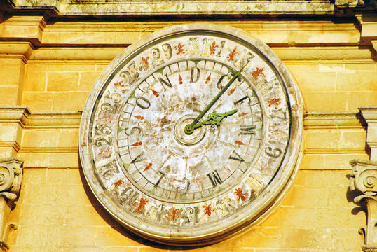 Old wall clock with numeric and alphabetic dial on a building in Mdina, Malta.