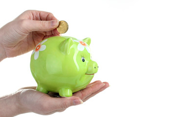 a woman throws a gold coin into a green piggy Bank isolated on white background