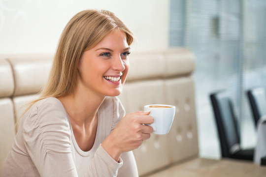 Young happy woman drinking coffee in a cafe