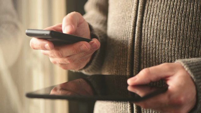 Smartphone and tablet data synchronization, man syncing files and documents on personal wireless electronic devices at home.