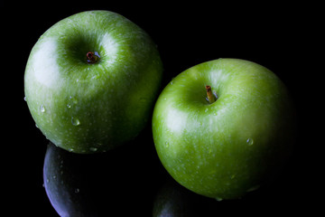 Two green fresh ripe apples on black background with reflection from high angle