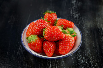 Ripe red strawberries in iron bowl on wooden background
