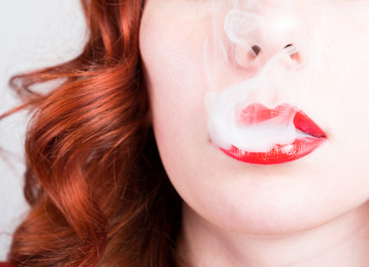 Fototapeta premium close-up portrait of a elegant young redhead woman, bright red lips, the smoke releases