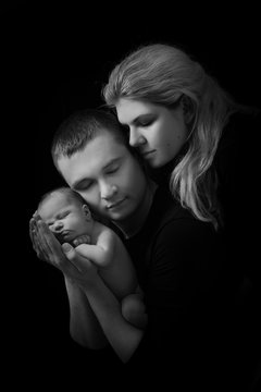 happy family , young parents holding a newborn baby in her arms and gently hugged him, black and white photo on a black background .