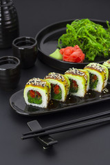 Vegetarian sushi roll with avocado ginger wasabi and chuka salad over black background