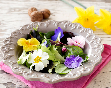 close up of spring salad with edible flowers over white rustic w