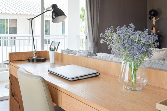 wooden table with computer notebook,pencil,lamp and artificial flowers in modern working area at home