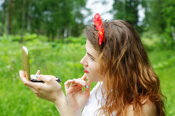 Girl with a bow on her head looking into the mirror on the natur