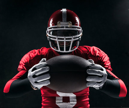American football player posing with ball on black background