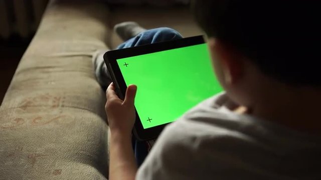 Child using a digital tablet PC with green screen, back view