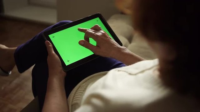 Aged woman using a digital tablet PC with green screen, back view