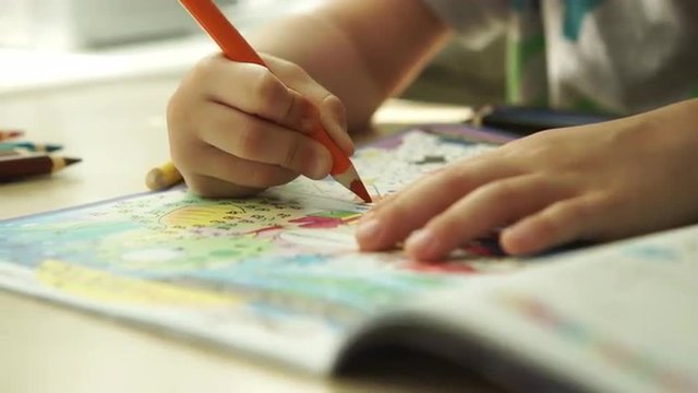 TRACKING: Child hands paints a orange pencils on a paper