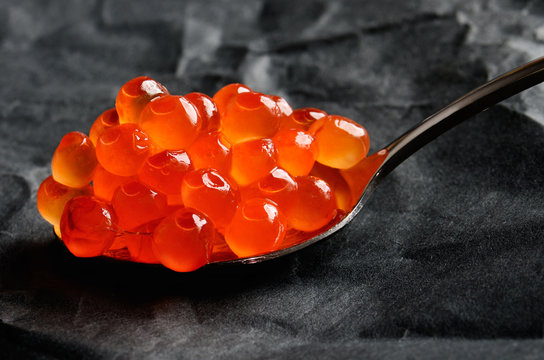 Red caviar in a metal spoon on a dark grey background