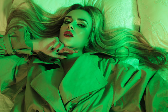 beautiful girl in the coat with red lips on the bed with green light