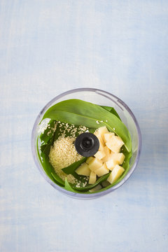 Food processor bowl with ingredients for pesto sauce: wild garlic, sesame seeds, olive oil and parmesan cheese