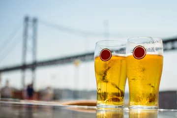 Fotobehang Two glasses of light beer on the background of suspension bridge. The glasses have spaces for logo. © oleksii.leonov