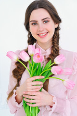 Beautiful young woman smiling happily and holding a bunch of delicate spring pink tulips in front of her