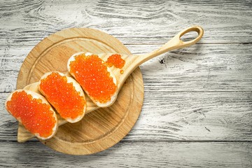 Sandwiches with salmon red caviar on a cutting boards and natural wooden background with copy space
