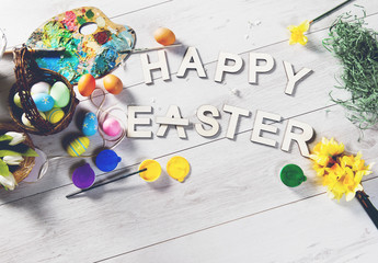 Colored eggs and other decorations on a white wooden table with HAPPY EASTER sign, Easter background