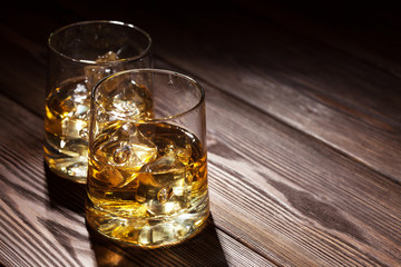 Glasses of whiskey with ice on wood