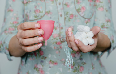 Woman holding tampons and menstrual cup in hands