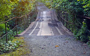 Старый железный мост с кривыми перилами через заросший овраг