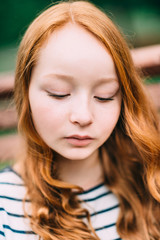 Close-up portrait of lovely thoughtful girl with long curly red hair in summer park. Outdoor portrait of a red-haired teenage girl. Adorable young redhead longhaired woman