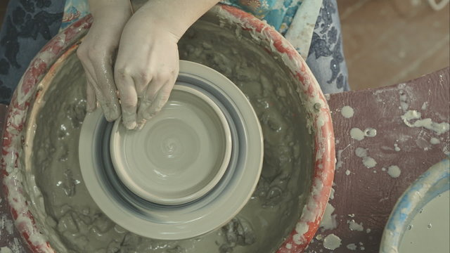 Hands of a woman creating a clay jar on a potter's wheel. RAW video record.