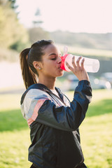 Young hispanic woman drinking water after running