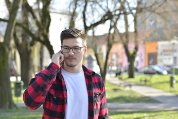 Outdoor portrait of modern young man with mobile phone in park